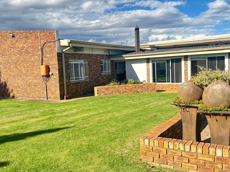 Rear view of the property featuring a face-brick facade, a well-maintained lawn, and a swimming pool with a brick-paved surround.