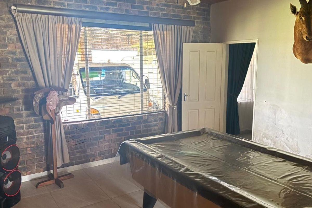 Living area featuring exposed brickwork, tiled flooring, and a window with security bars. The wall shows signs of moisture damage requiring attention.