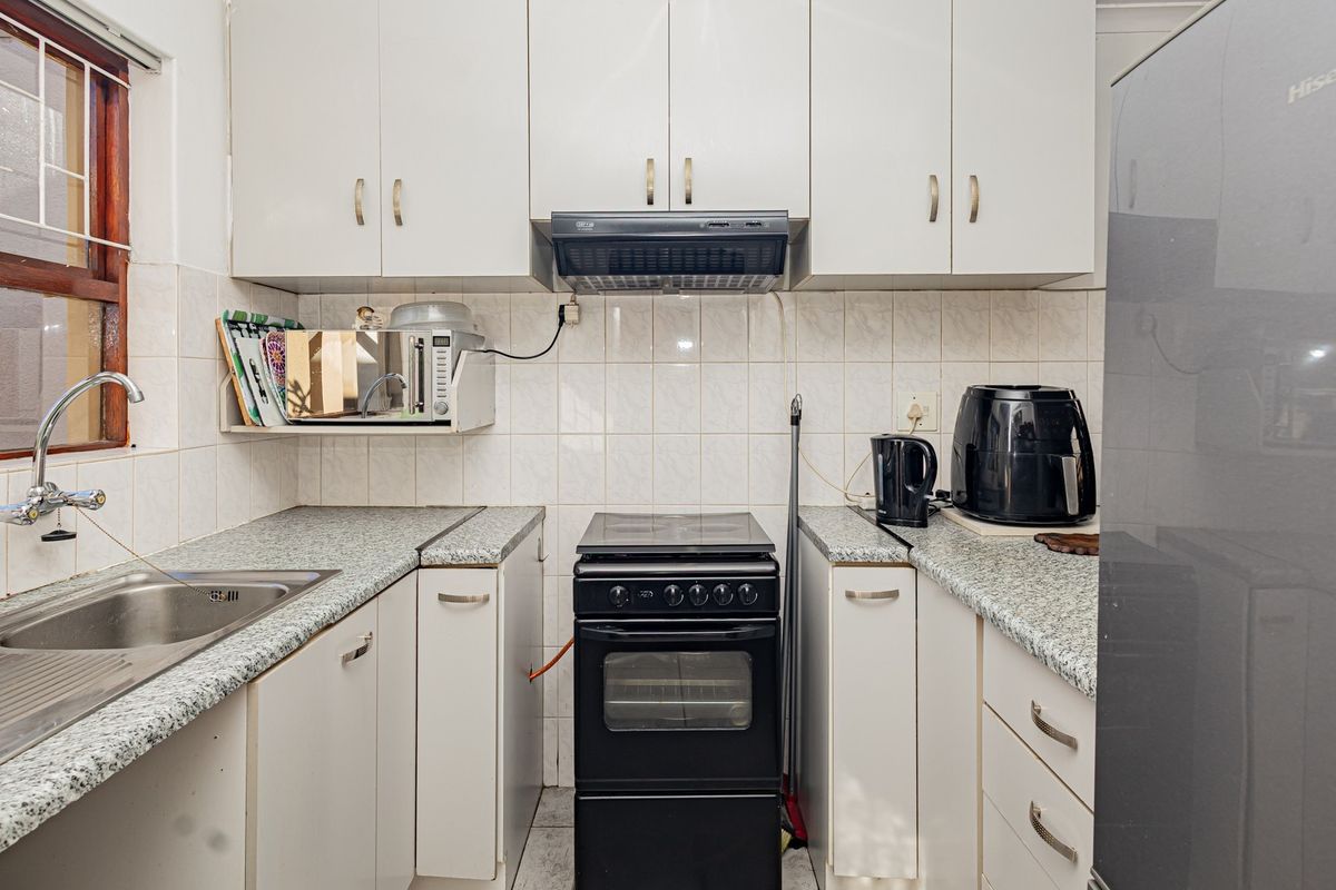A functional kitchen featuring white cabinetry, laminate countertops, a tiled splashback, and a freestanding stove with an overhead extractor fan.