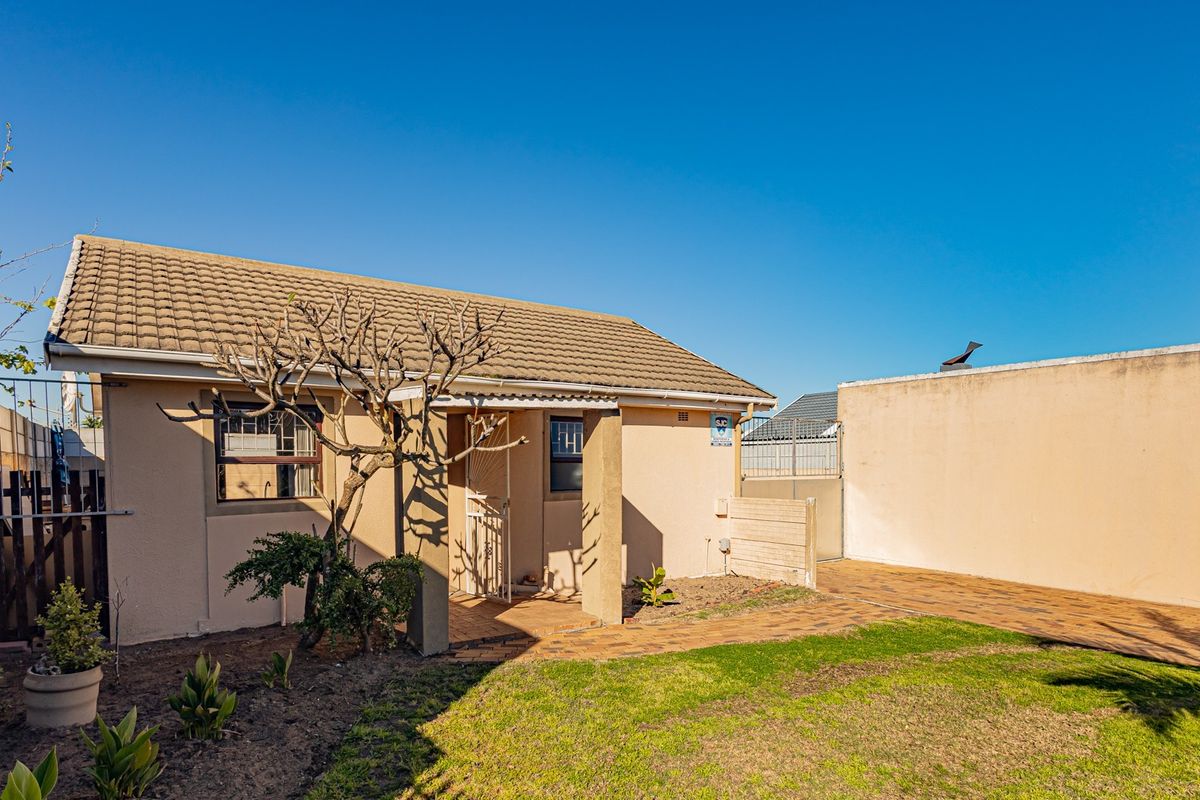 Rear view of the property featuring a tiled roof, paved driveway, and a secure boundary wall with a small garden area.