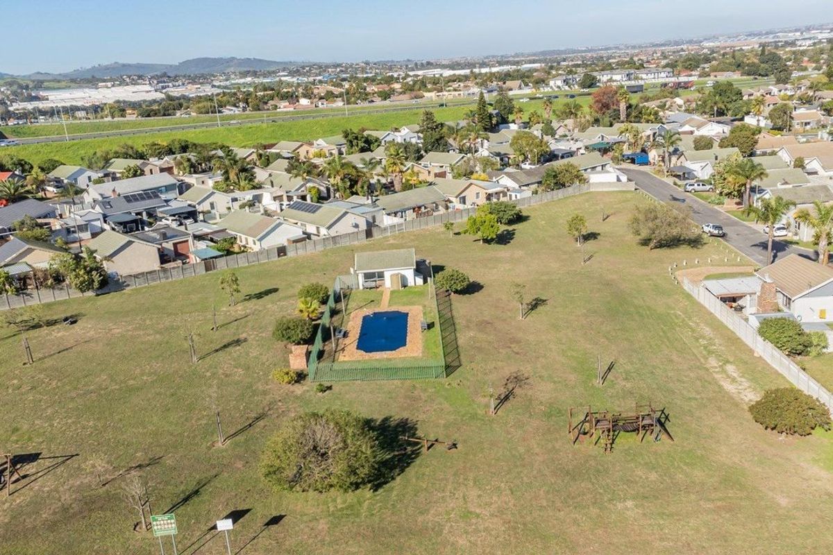 Aerial view of a residential property featuring a swimming pool with safety fencing, a small outbuilding, and a large surrounding garden area.