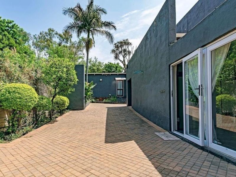 A paved rear courtyard area featuring modern dark grey exterior walls and large sliding glass doors providing access to the home.