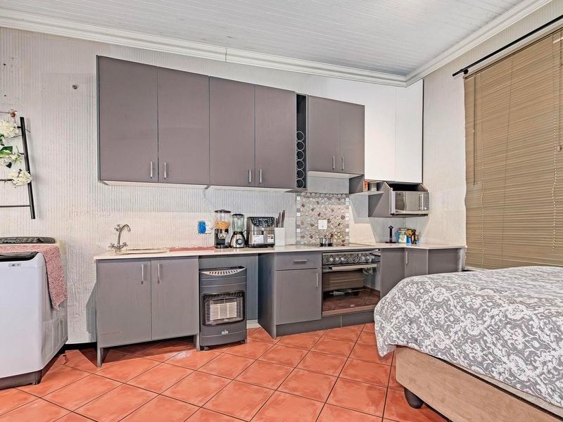 Compact kitchen area featuring grey cabinetry, mosaic backsplash, built-in oven, and tiled flooring, integrated within a multi-purpose living space.