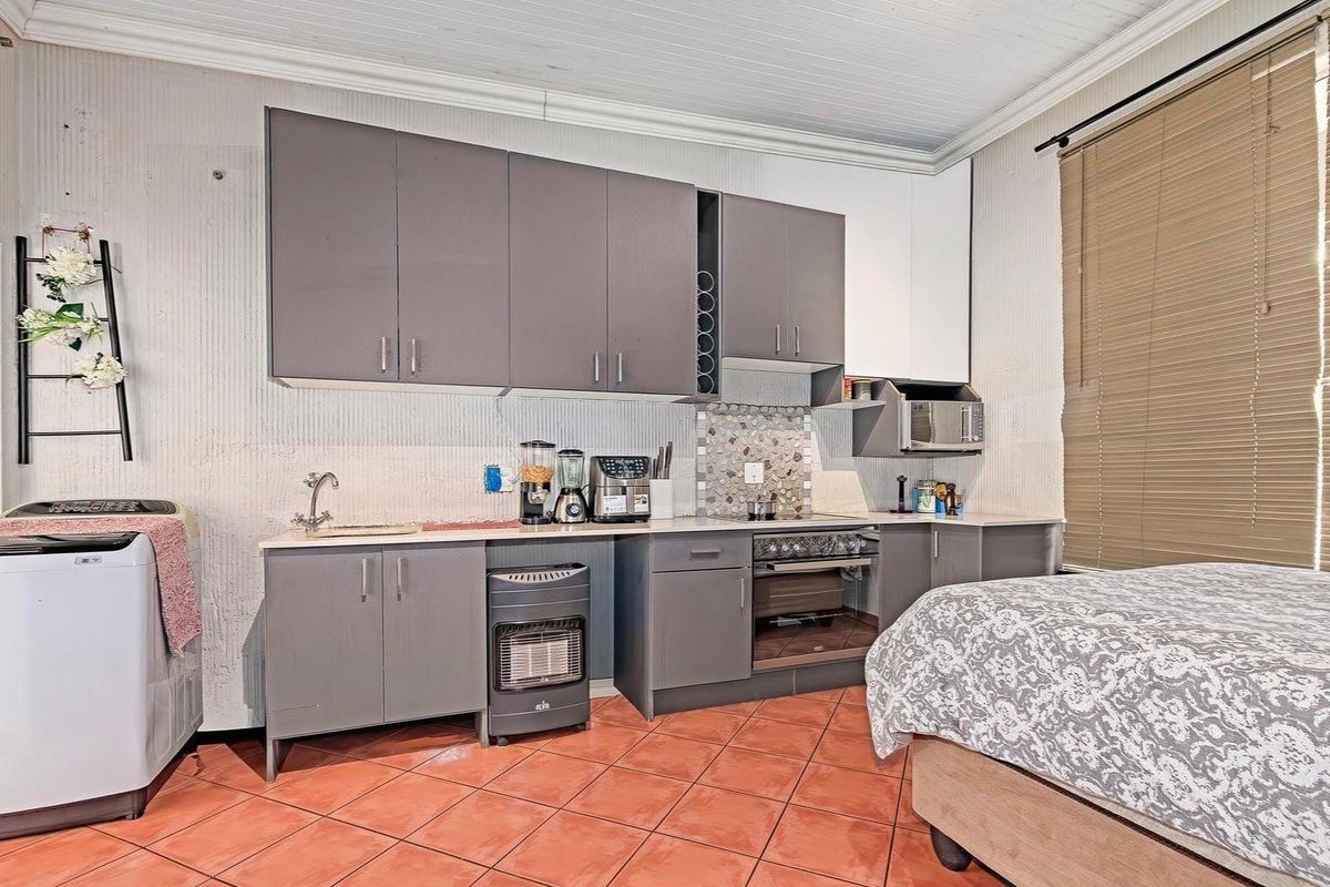 Compact kitchen area featuring grey cabinetry, mosaic backsplash, built-in oven, and tiled flooring, integrated within a multi-purpose living space.