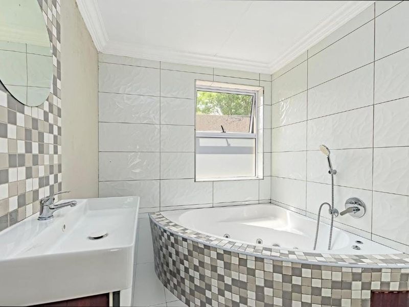 A bright bathroom featuring a corner bathtub with handheld shower, a modern basin, and decorative mosaic tile accents.