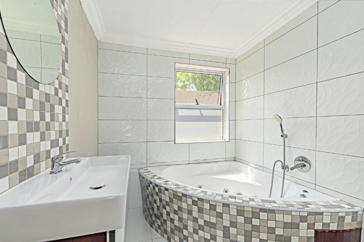 A bright bathroom featuring a corner bathtub with handheld shower, a modern basin, and decorative mosaic tile accents.