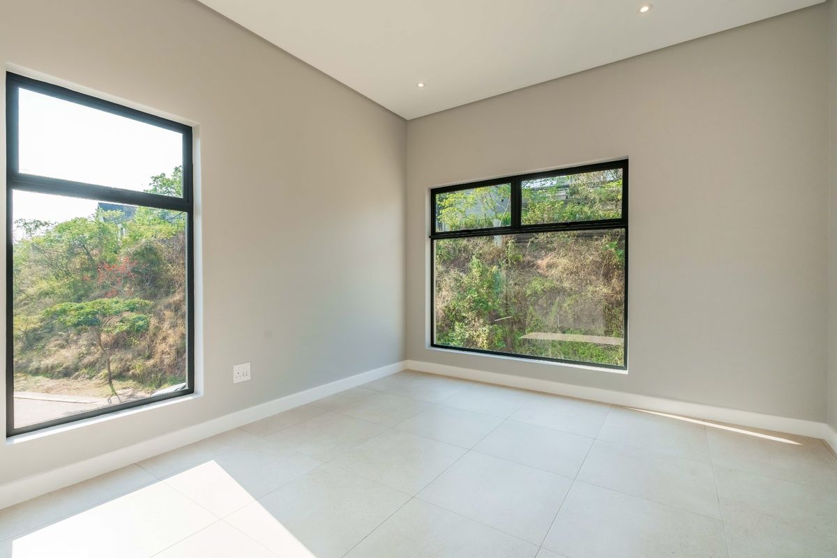 A bright, modern, and empty bedroom featuring large windows with natural views, neutral wall tones, and clean tiled flooring.