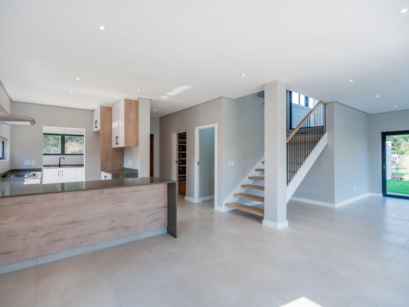 Modern open-plan living area featuring a sleek kitchen with stone countertops, gas hob, and a timber staircase leading to the upper level.