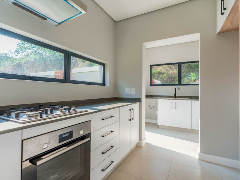 Modern kitchen featuring sleek white cabinetry, stone countertops, gas hob, built-in oven, and an adjoining scullery area with a sink.