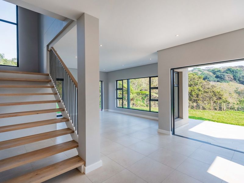 Spacious open-plan living area featuring modern timber staircase, large format floor tiles, and seamless indoor-outdoor flow through sliding glass doors to the garden.