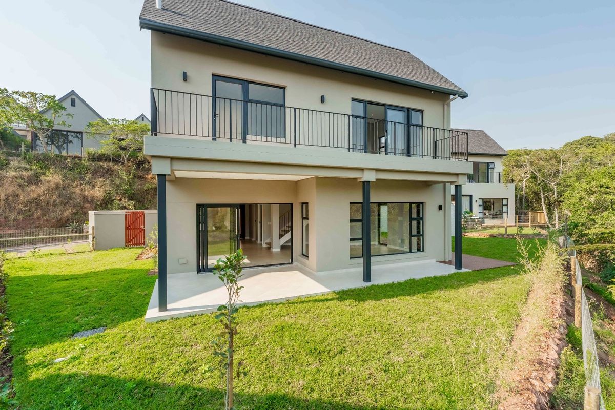 Rear view of a modern two-story house featuring a ground-floor patio, an upper-level balcony with metal railings, and a well-maintained garden.