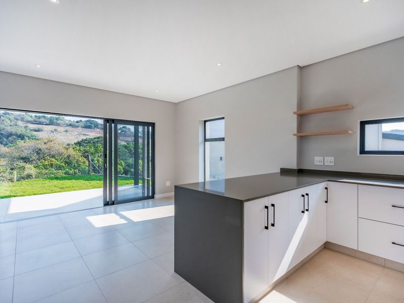 Modern open-plan kitchen and living area featuring sleek white cabinetry, stone countertops, and large sliding doors opening to a landscaped garden view.