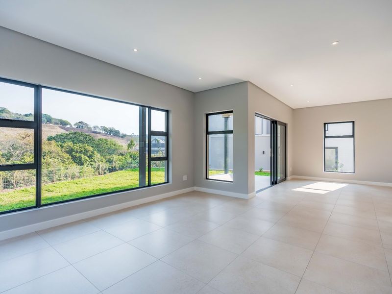 Spacious, modern open-plan living area featuring large format floor tiles, recessed lighting, and expansive windows with scenic views and direct outdoor access.