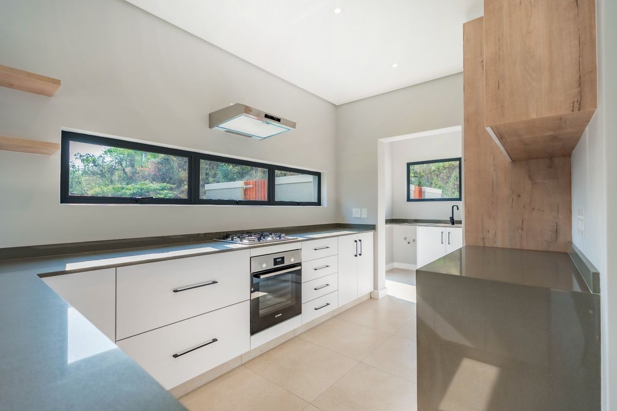 Modern kitchen featuring sleek white cabinetry, stone countertops, built-in oven, gas hob, and an adjoining scullery area with neutral tiled flooring.