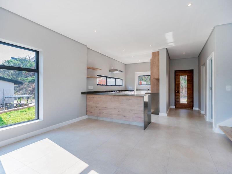 Modern open-plan kitchen and living area featuring sleek cabinetry, a central island, tiled floors, and abundant natural light through large windows.