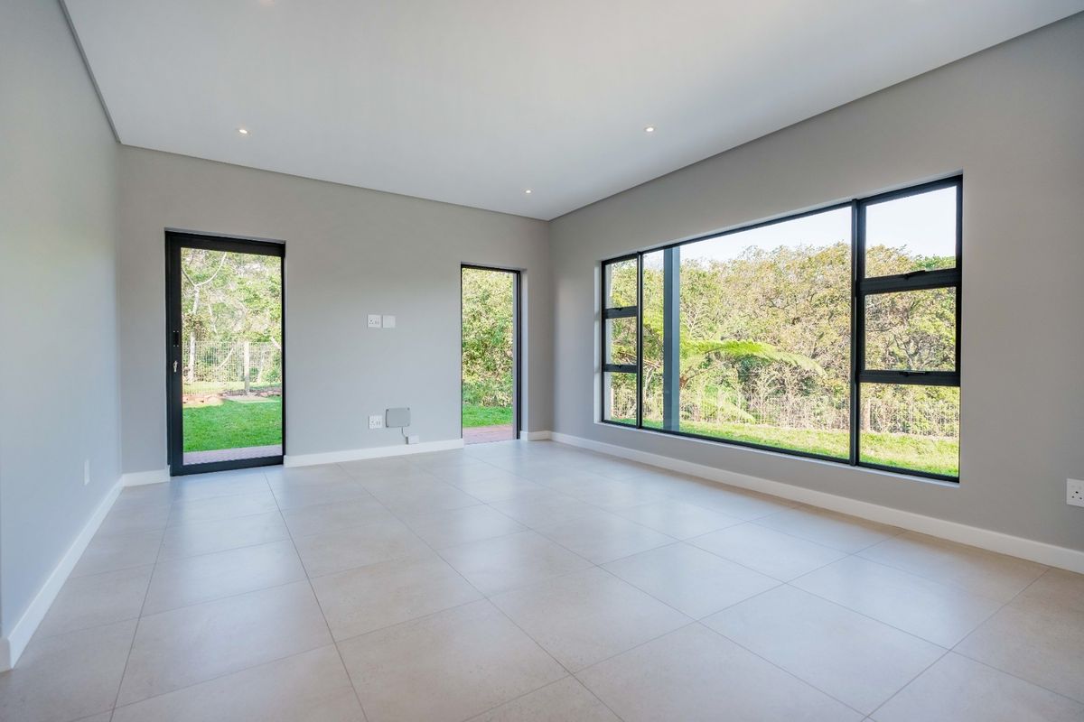 A bright, modern, and spacious living area featuring large format floor tiles, recessed lighting, and expansive windows with views of the surrounding greenery.