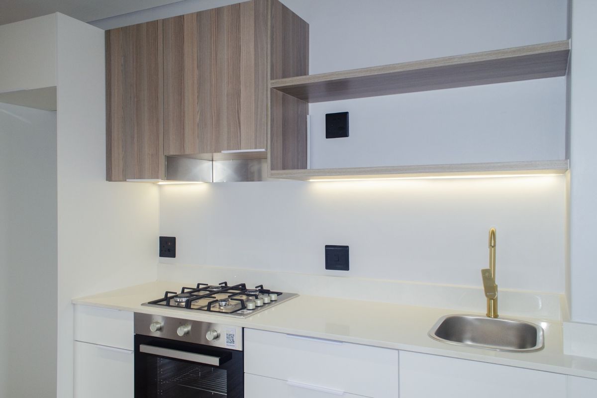 Modern kitchen featuring white cabinetry, quartz countertops, a gas hob, built-in oven, and elegant brass fixtures with integrated under-cabinet lighting.