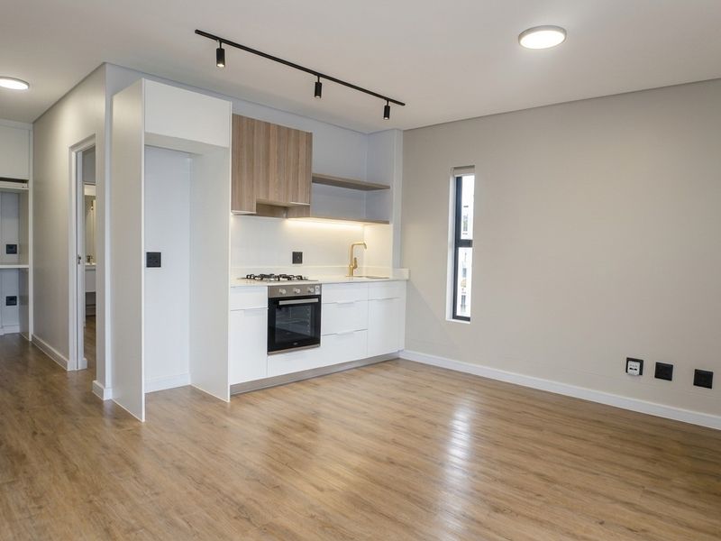Modern open-plan kitchen featuring sleek white and wood-tone cabinetry, integrated appliances, and high-quality laminate flooring in a bright, contemporary living space.