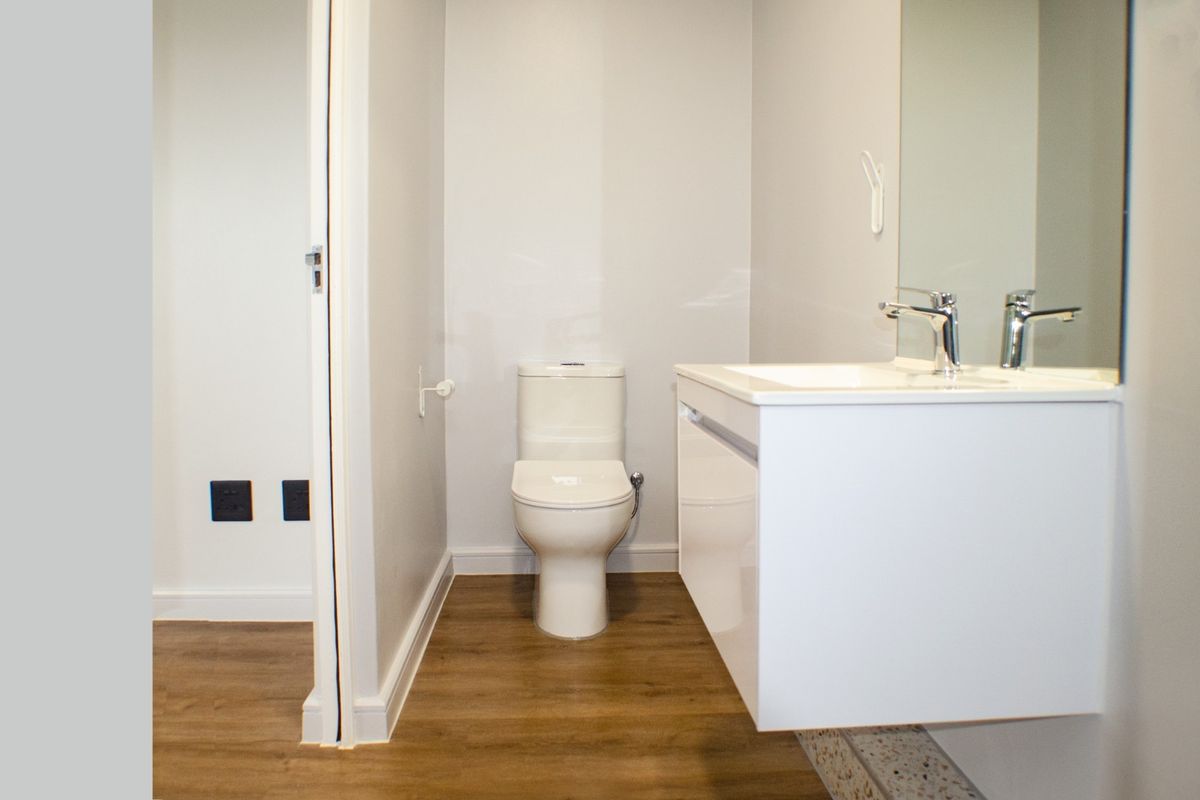 A modern, clean bathroom featuring a wall-mounted vanity with basin, mirror, and toilet, finished with contemporary laminate flooring.