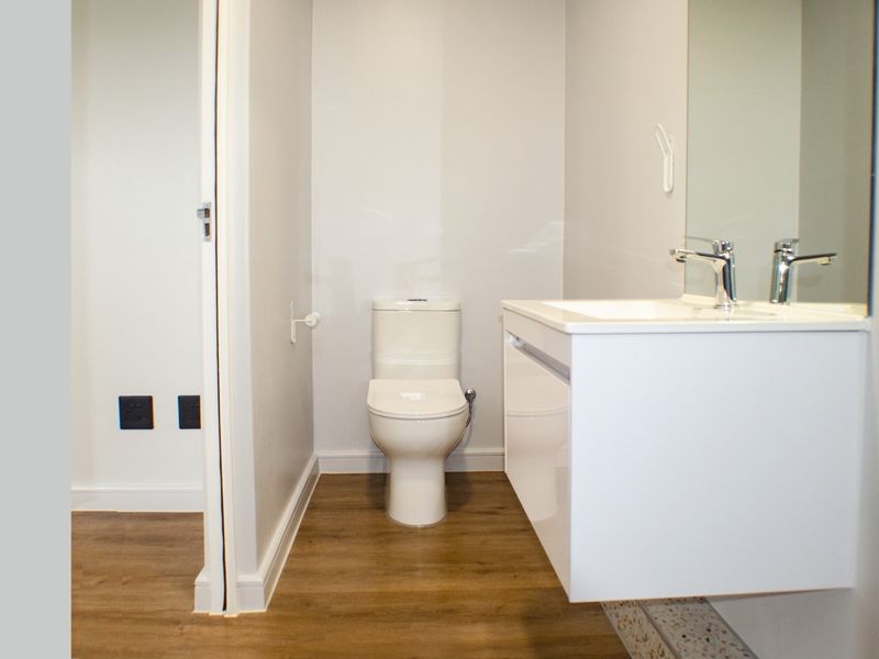 A modern, clean bathroom featuring a wall-mounted vanity with basin, mirror, and toilet, finished with contemporary laminate flooring.