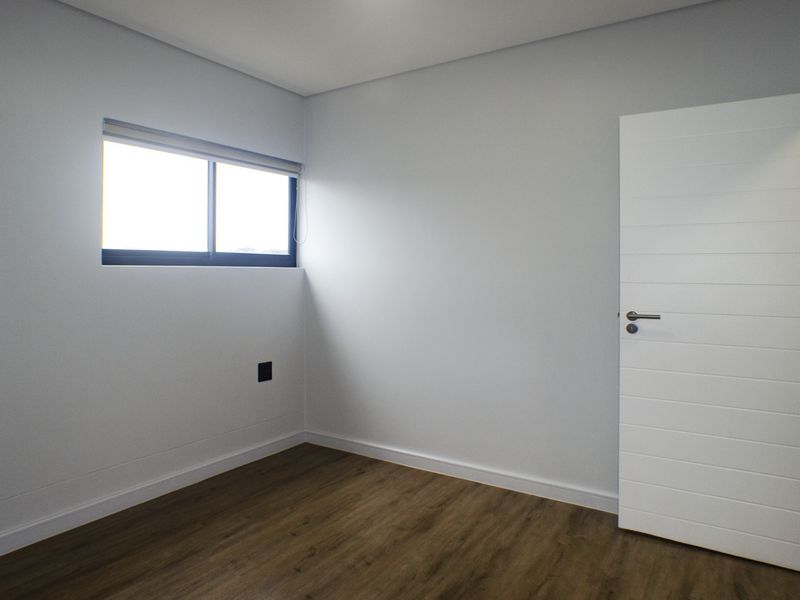 A clean, empty bedroom featuring modern laminate flooring, neutral walls, and a sliding window, providing a blank canvas for personalization.
