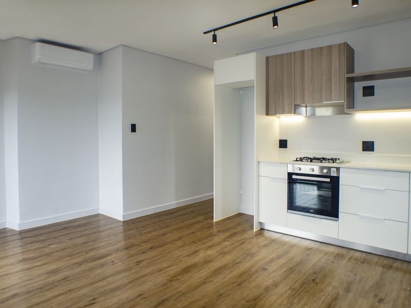 Modern open-plan living area featuring a sleek kitchen with built-in appliances, track lighting, and wood-look laminate flooring throughout.