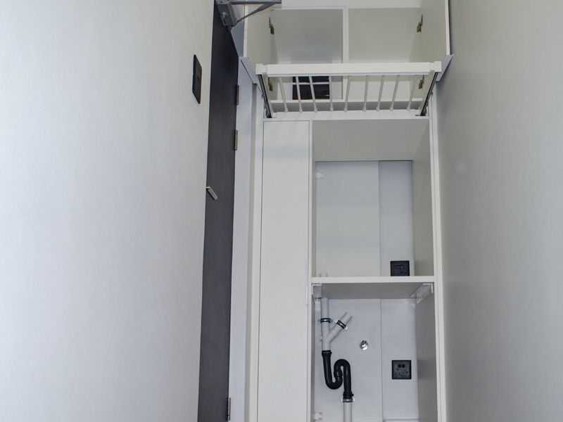 A compact, dedicated laundry utility space featuring built-in cabinetry with integrated plumbing and electrical connections for a washing machine.