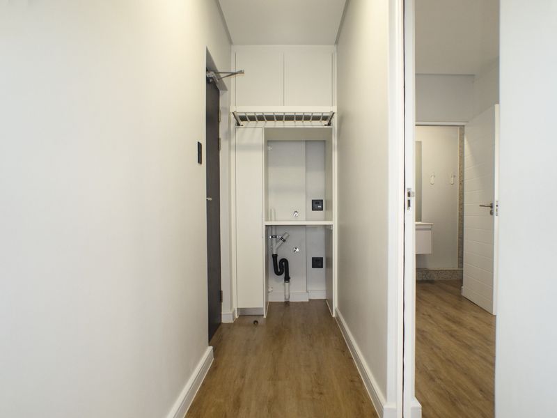 A clean, functional laundry nook featuring built-in cabinetry and plumbing connections, situated within a hallway area with modern laminate flooring.