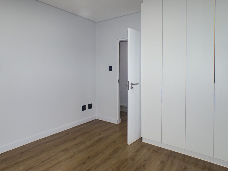 A clean, modern bedroom featuring light-toned laminate flooring and a large, white built-in wardrobe with ample storage space.