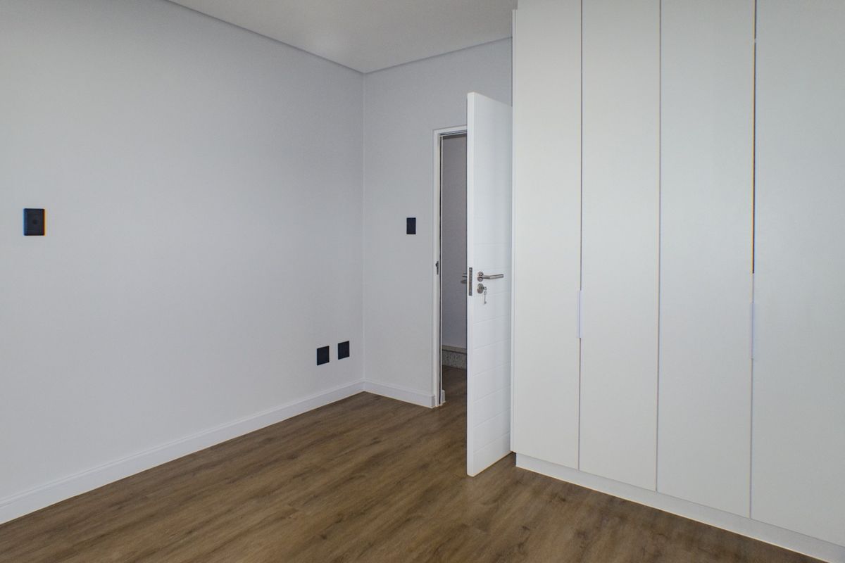 A clean, modern bedroom featuring light-toned laminate flooring and a large, white built-in wardrobe with ample storage space.