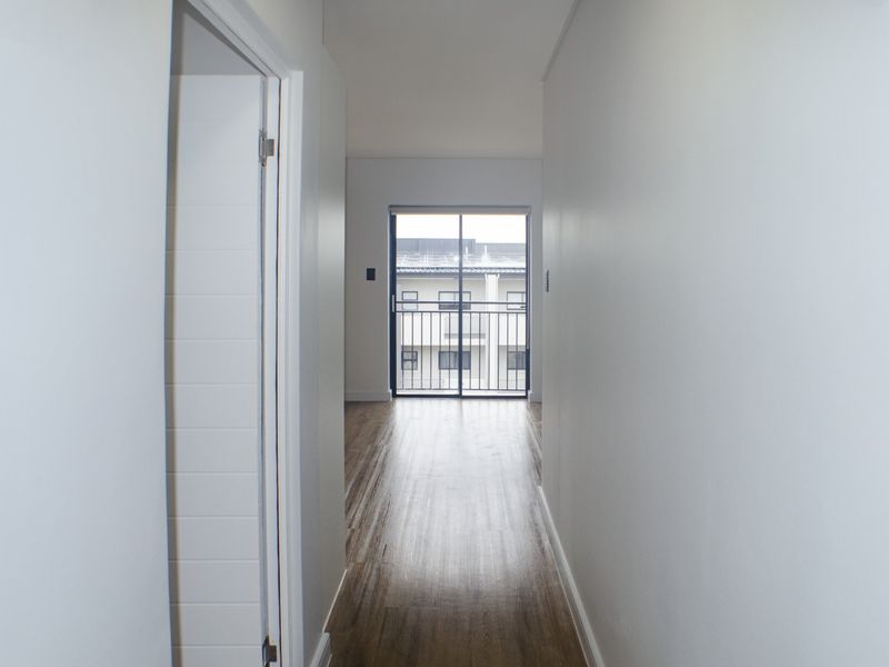 A clean, empty hallway with modern laminate flooring leading towards a sliding glass door that opens onto a balcony.