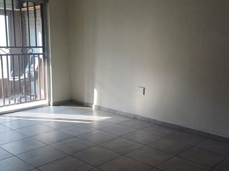 An empty living room featuring neutral floor tiles, a sliding door with a security gate, and natural light, ready for personalization.
