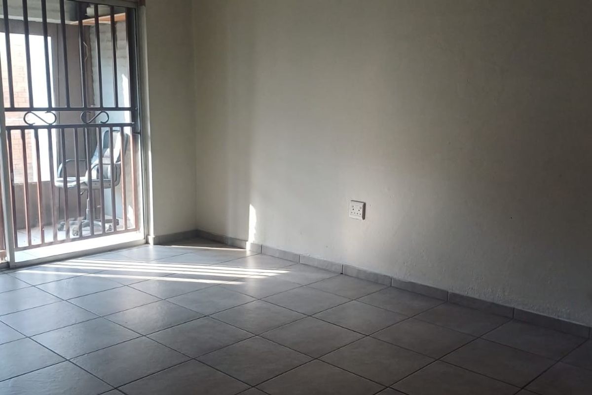 An empty living room featuring neutral floor tiles, a sliding door with a security gate, and natural light, ready for personalization.