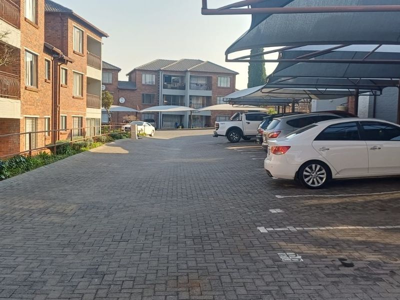 Exterior view of a townhouse complex featuring a paved driveway and covered parking bays for residents.