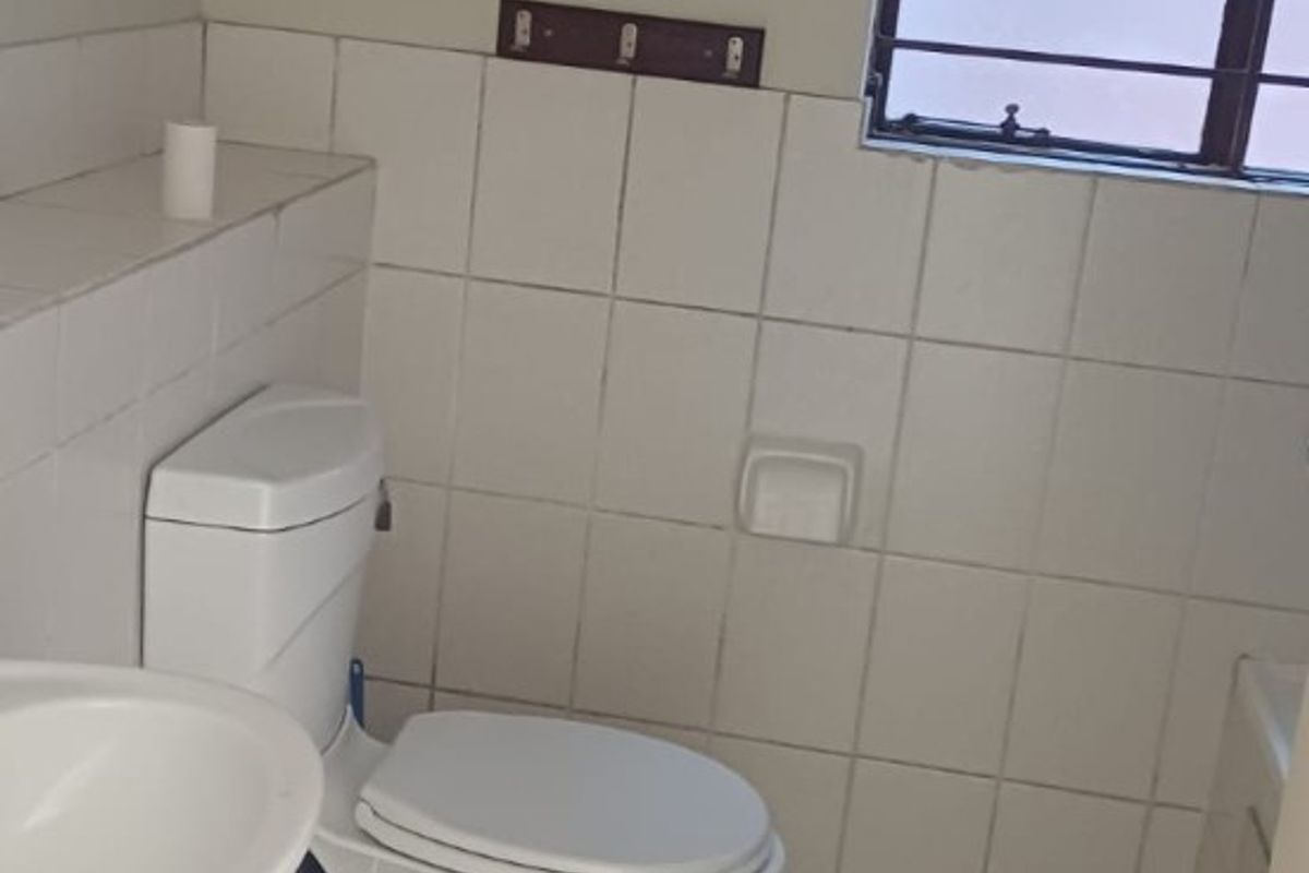 A functional bathroom featuring a pedestal basin, toilet, and tiled finishes, offering a clean and simple layout ready for potential cosmetic updates.