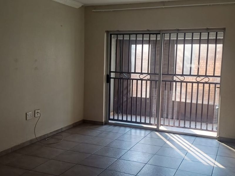 An empty living room featuring tiled flooring and a sliding glass door with an integrated security gate, providing access to the exterior.