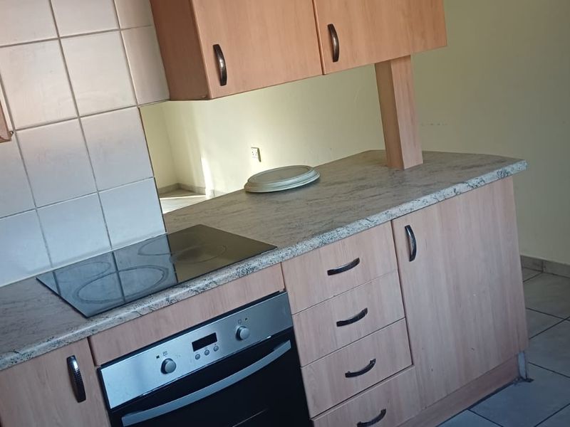 A functional kitchen featuring laminate cabinetry, a stone-look countertop, built-in electric oven, and hob, finished with ceramic floor tiles.