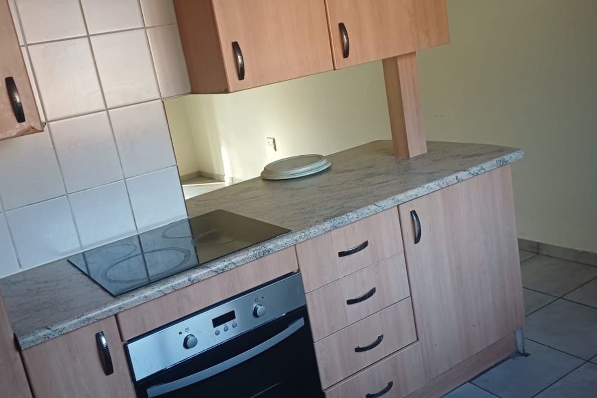 A functional kitchen featuring laminate cabinetry, a stone-look countertop, built-in electric oven, and hob, finished with ceramic floor tiles.