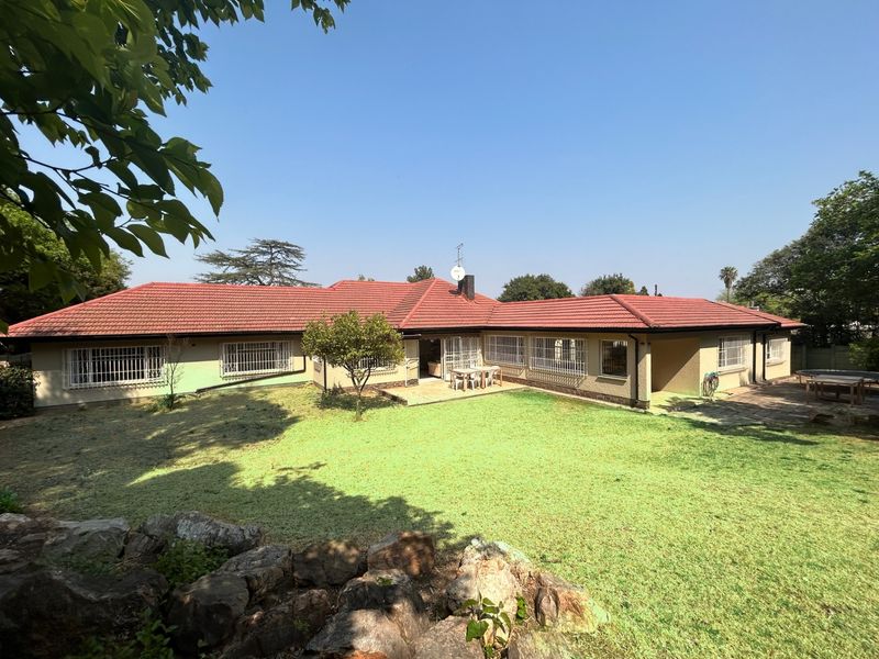 Rear view of a single-story house featuring a tiled roof, security bars on windows, and a paved patio area overlooking a spacious garden.