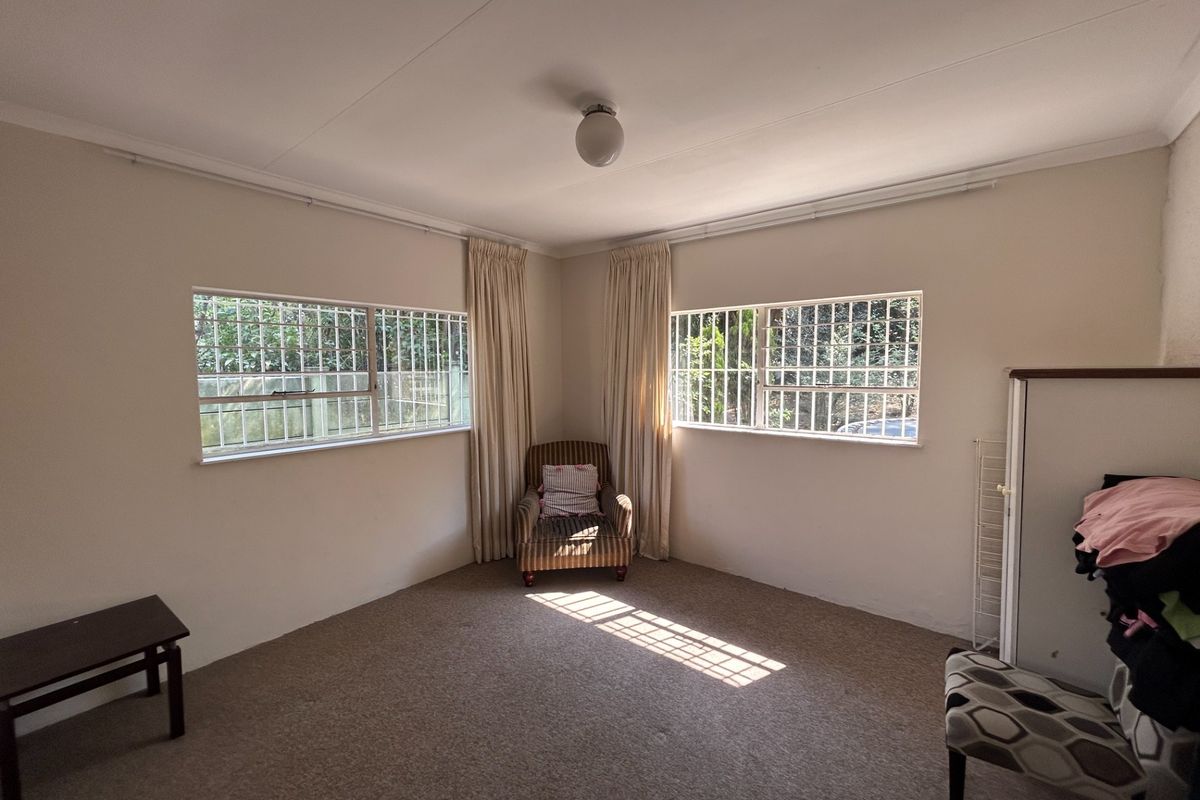 A neutrally painted bedroom featuring carpeted flooring, security bars on the windows, and ceiling-mounted lighting, offering a blank canvas for personalization.