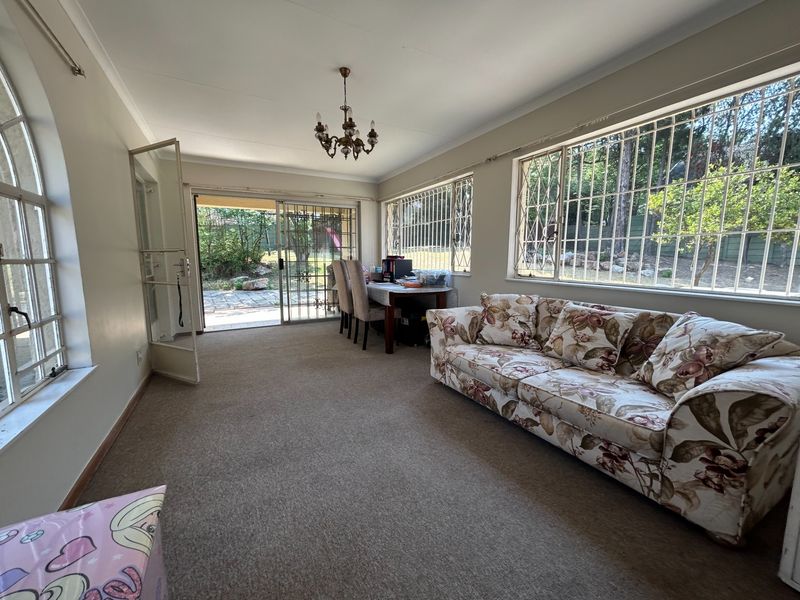 Spacious living area featuring large windows with security bars, carpeted flooring, and direct access to the rear garden through a sliding glass door.