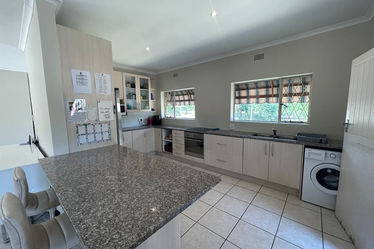 A functional kitchen featuring granite countertops, built-in cabinetry, an integrated oven and hob, and tiled flooring with ample natural light.