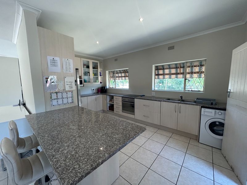 A functional kitchen featuring granite countertops, built-in cabinetry, an integrated oven and hob, and tiled flooring with ample natural light.