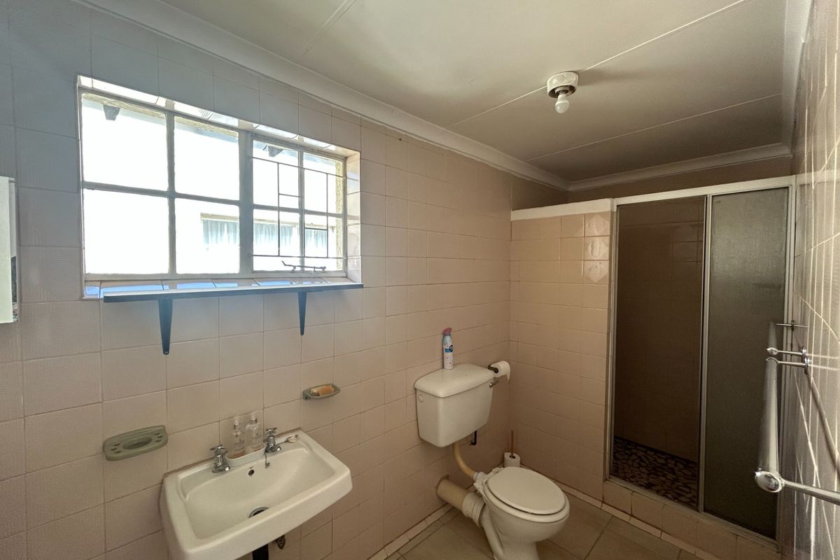 A dated bathroom featuring a wall-mounted basin, toilet, and a separate shower enclosure with tiled finishes throughout.