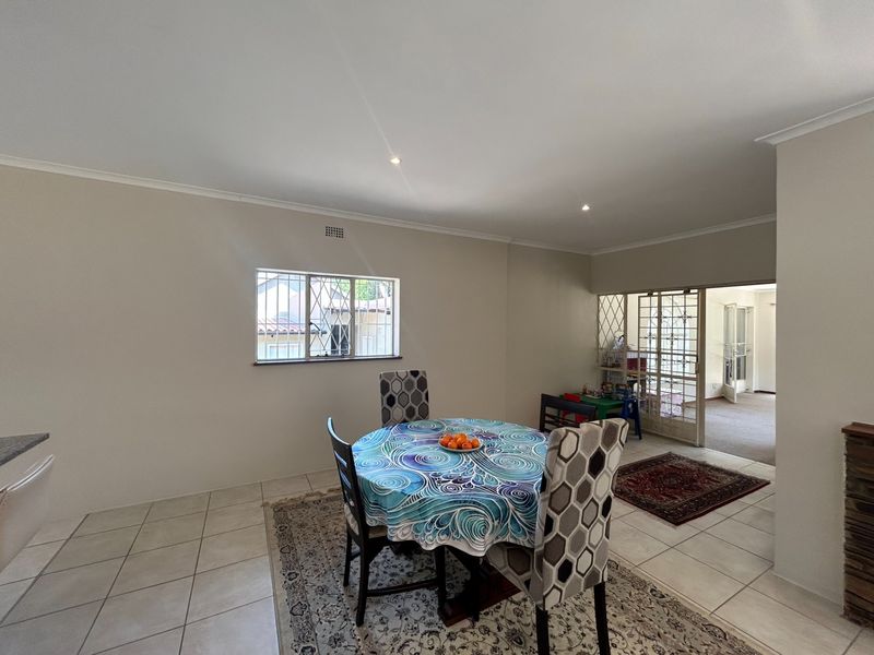 A neutrally painted living area featuring tiled flooring, recessed downlights, and a security gate leading to an adjacent room.