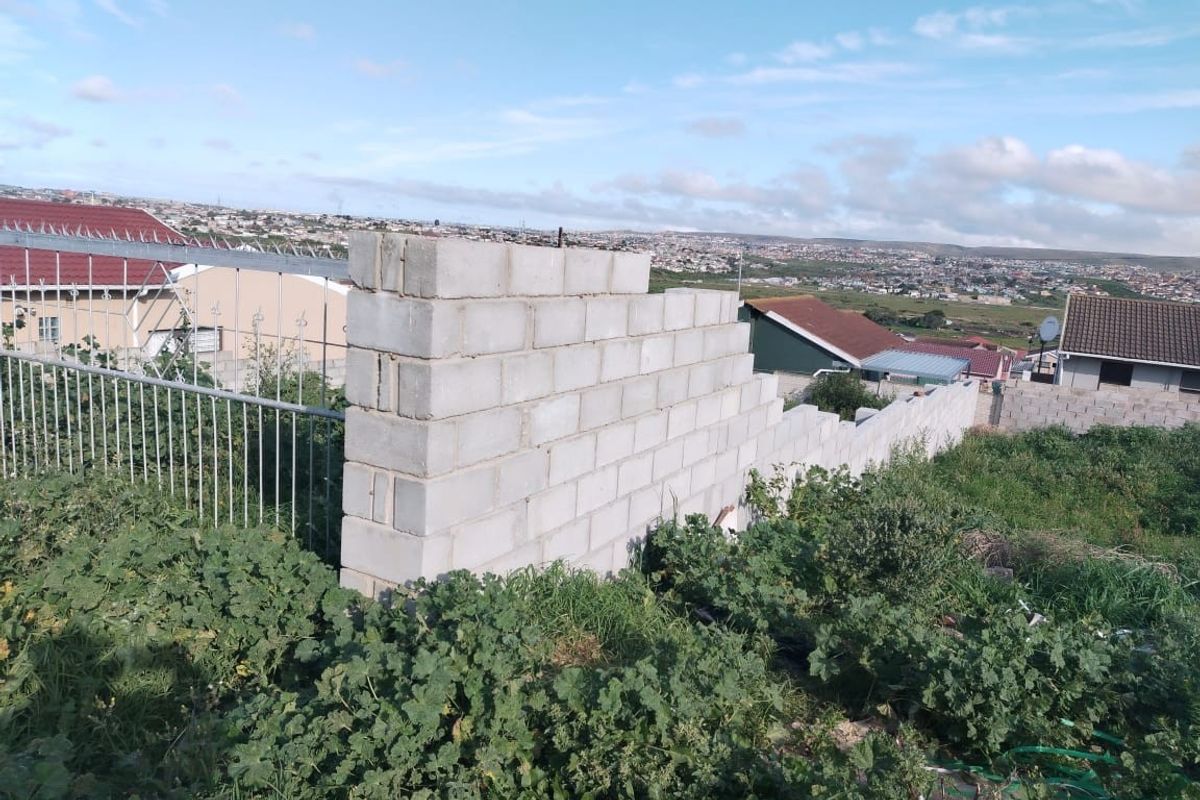 A view of an unfinished concrete block boundary wall on a vacant residential plot with surrounding neighborhood views.
