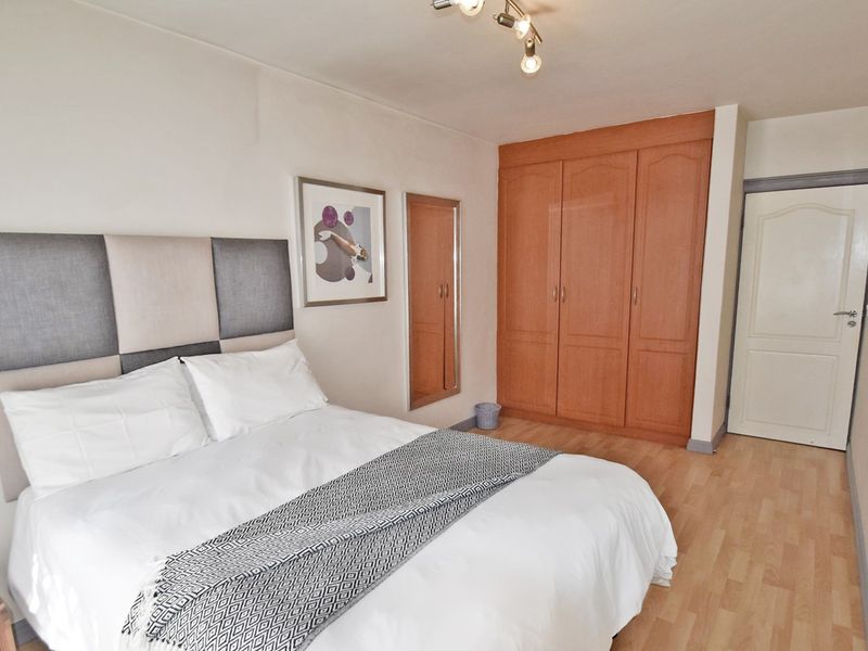 A bedroom featuring laminate flooring, a built-in wooden wardrobe, and a ceiling light fixture.