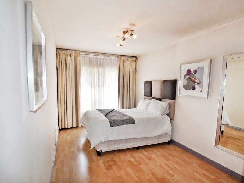 A well-maintained bedroom featuring laminate flooring, neutral walls, and large windows with curtain tracks, providing a bright and comfortable living space.