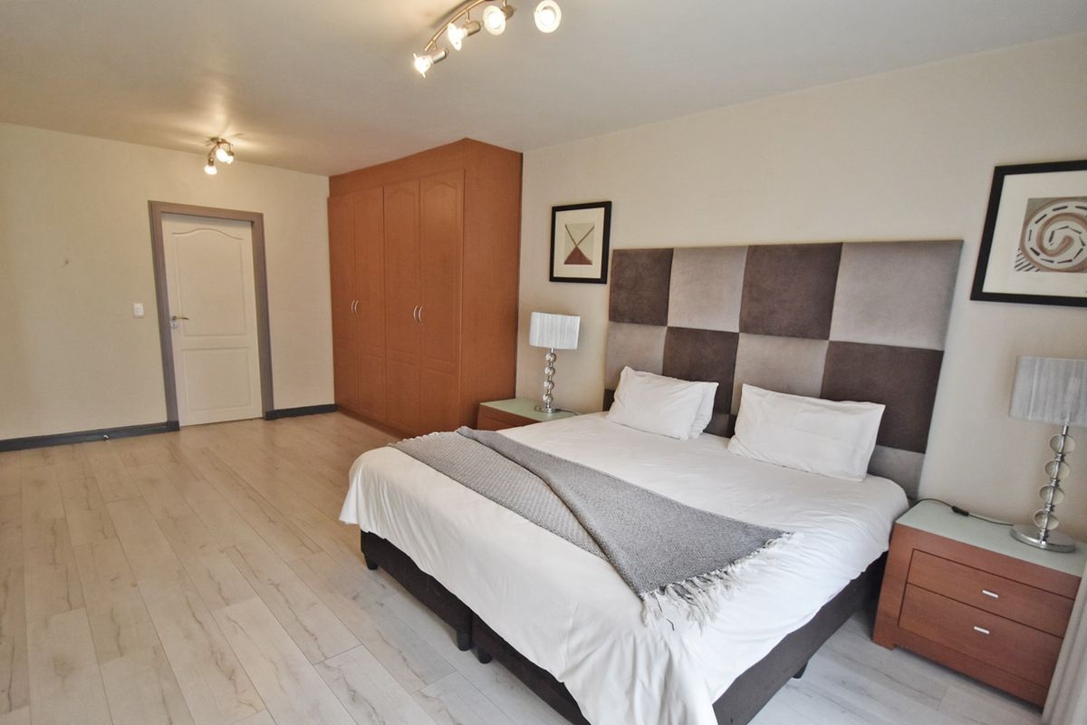 Spacious bedroom featuring light-toned laminate flooring, a large built-in wardrobe, and modern track lighting.
