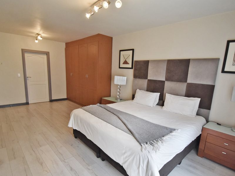 Spacious bedroom featuring light-toned laminate flooring, a large built-in wardrobe, and modern track lighting.